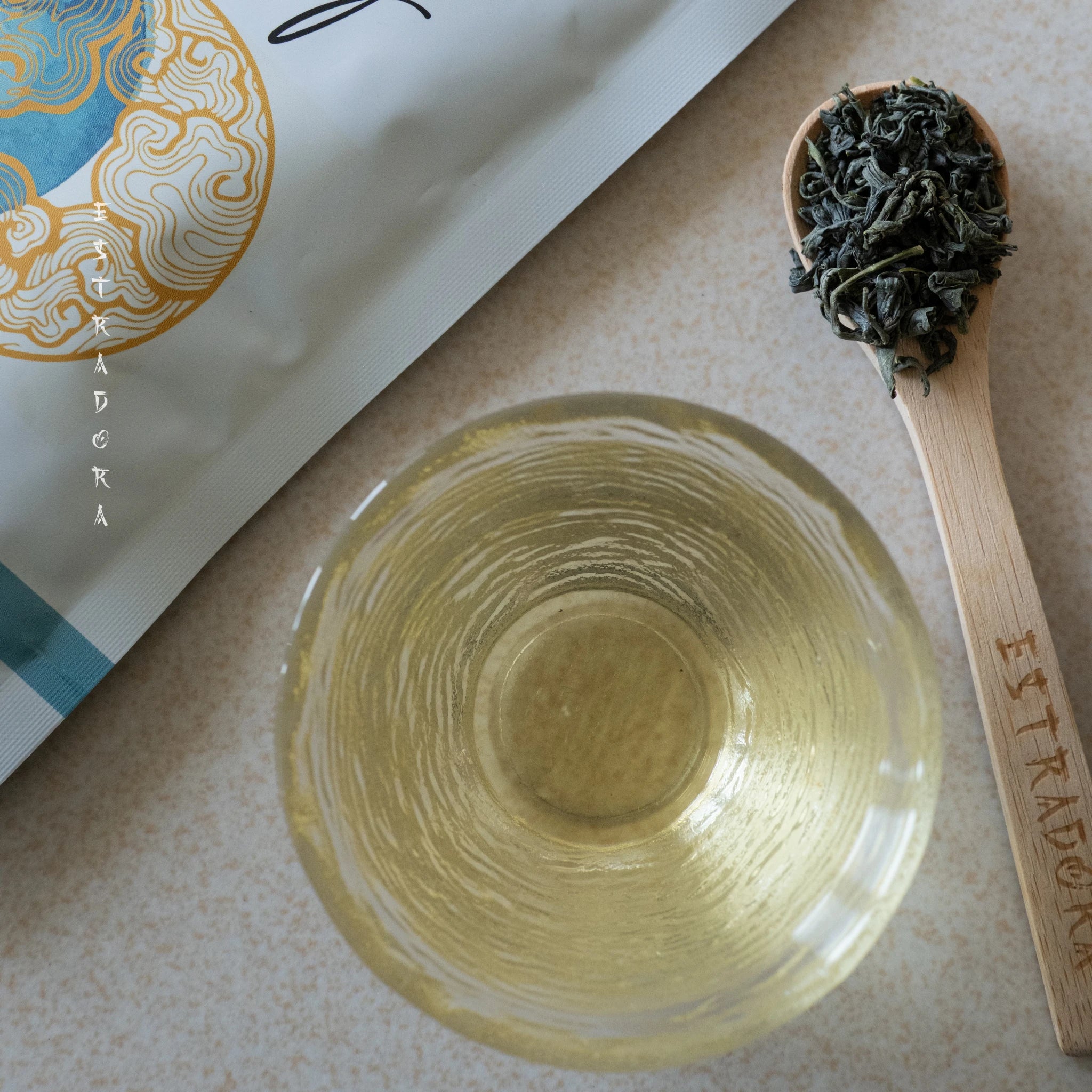Brewed Japanese Oolong green tea in glass cup with loose leaves on wooden spoon – ceremonial grade - Estradora