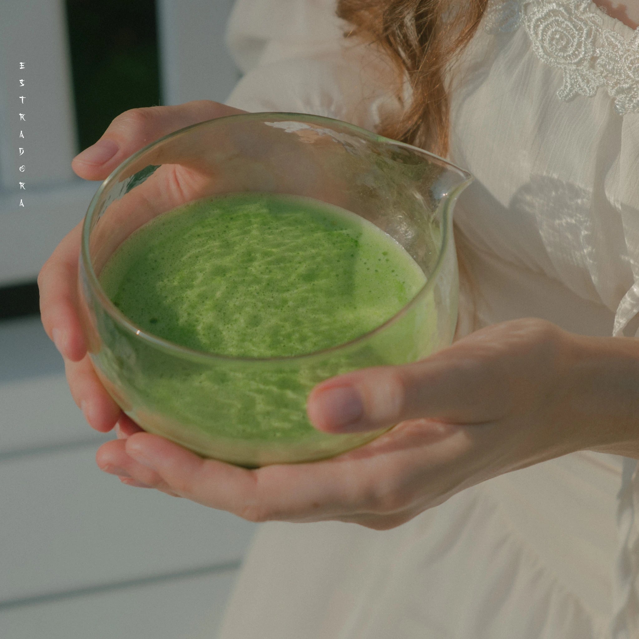 Hands holding glass chawan with ceremonial matcha tea - Estradora