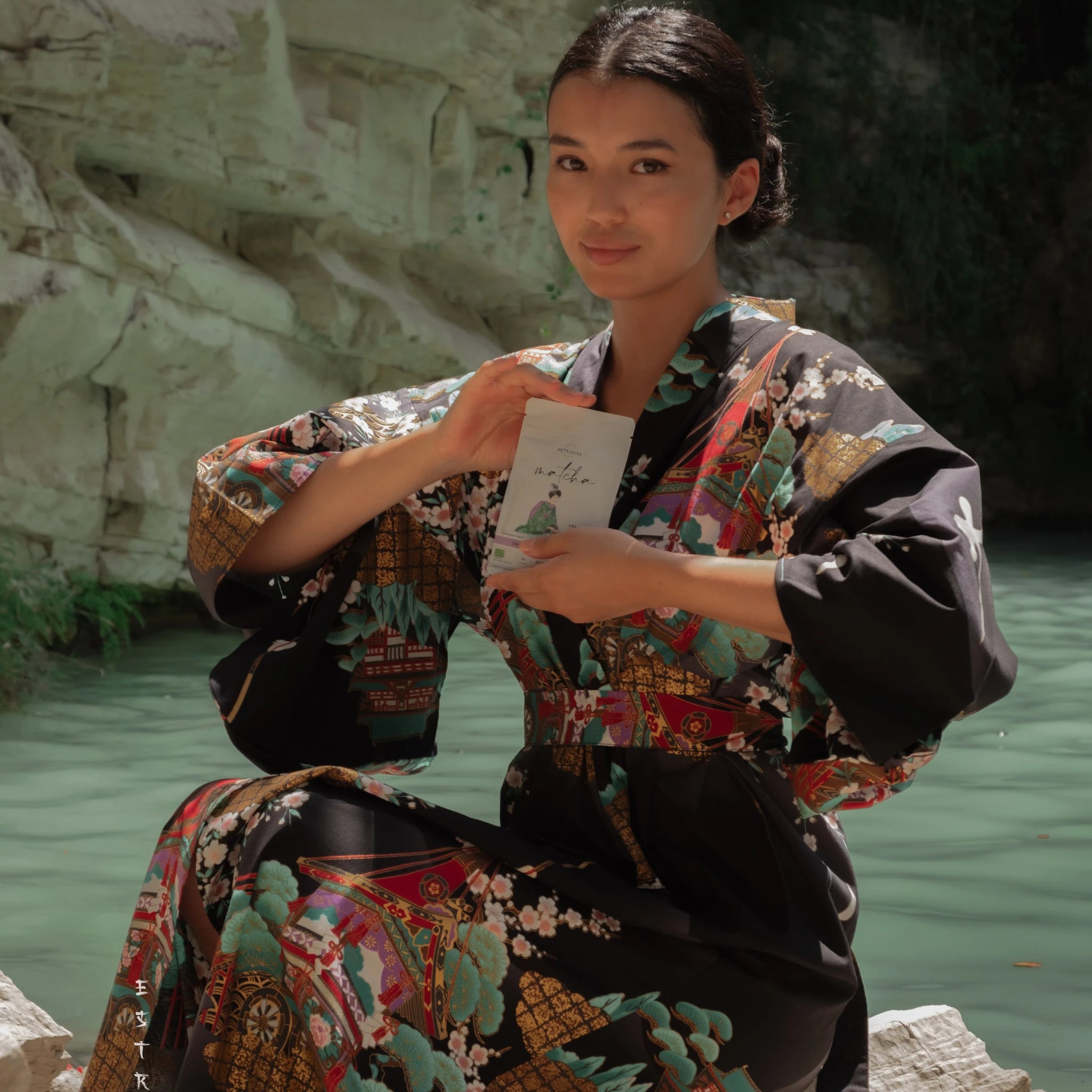 Woman in traditional kimono sitting by the water, holding a package of Japanese matcha Estradora